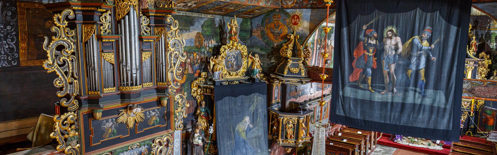 Wnętrze kościoła. Belka tęczowa oraz ołtarz boczny zasłonięte dużymi ciemnymi płótnami. Na jednym z nich namalowano scenę biczowania Chrystusa, na drugim Marie Magdalenę.