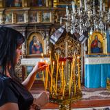 Wnętrze cerkwi, w tle ikonostas, na pierwszym planie kobieta zapalająca świece.