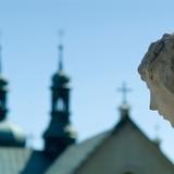 Sanktuarium w Czernej. Na pierwszym planie głowa rzeźby. W dali rozmyte dachy i wieże klasztoru.