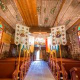 Wnętrze drewnianej cerkwi z ikonostasem, ławkami i chorągwiami.