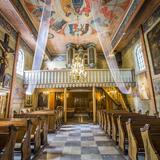 Wnętrze kościoła od strony wejścia. W centralnym punkcie chór z prospektem organowym, na ścianach wiszą obrazy (w tym stacje Drogi Krzyżowej), sufit pokrywa polichromia. Po obu stronach nawy stoją drewniane ławy.