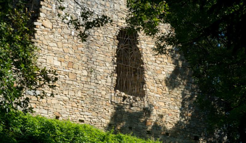 Ruiny zamku. Fragment kamiennej ściany z łukowatym oknem z kratą.