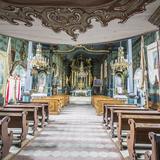 Wnętrze drewnianego kościoła w stylu rokokowym, polichromie, bogato złocony ołtarz, stylowe ławki.