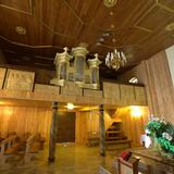 Skromne wnętrze drewnianego kościoła. Na głównym planie chór z prospektem organowym i rzeźbioną w drewnie balustradą. Po prawej widać fragment ołtarza i wiszący nad nim krzyż z Chrystusem.