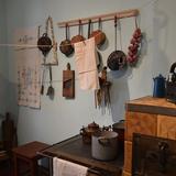 Piec kaflowy z garnkami, wiszące patelnie i ściereczki kuchenne. Piętro I kuchnia, fot. Maria Lempart.