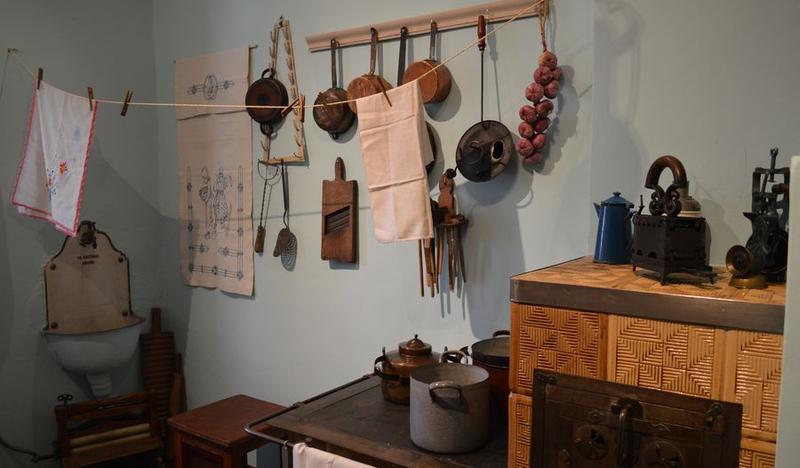 Piec kaflowy z garnkami, wiszące patelnie i ściereczki kuchenne. Piętro I kuchnia, fot. Maria Lempart.