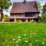 Drewniany kościół ze Szlaku Architektury Drewnianej w Lipnicy Murowanej w wiosennej scenerii. Obok rośnie zielona trawa z kwiatkami.