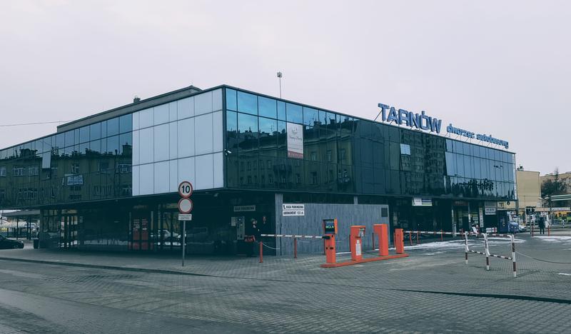 Zdjęcie przedstawia budynek Dworca autobusowego w Tarnowie. Na pierwszym planie widoczne bramki wjazdowe dla klientów w kolorze fluorescencyjnej pomarańczy.