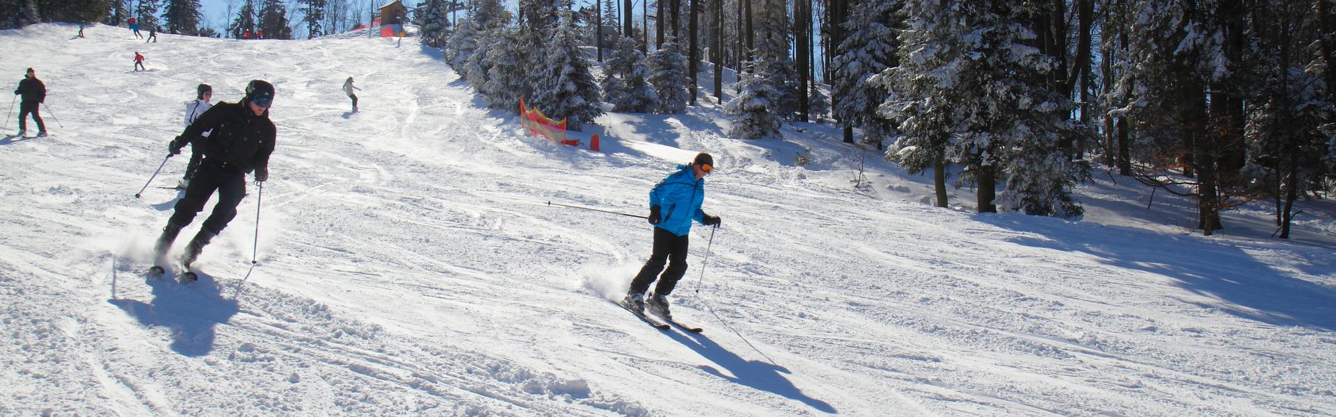 Widok na ośnieżony stok narciarski po ktorym jeżdza narciarze.