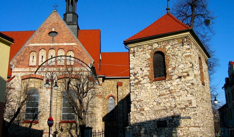 Duży, murowany kościół z kamienną dzwonią i czerwonymi dachami.