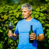 Na fotografii ujrzeć można mężczyznę ubranego podkoszulek koloru niebieskiego. W lewej ręce trzyma on butelkę z czerwonym winem, a w prawej widoczny napełniony już owym winem kieliszek. W tle rozmyte krzewy winorośli.