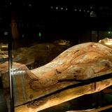 Drewniany sarkofag z mumią w gablocie ze szkła.