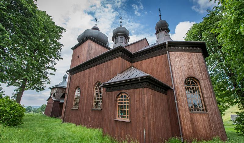Drewniana cerkiew oraz dzwonnica śród zieleni.
