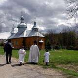 Drewniana cerkiew i idący do niej ludzie, duchowny z dziećmi w strojach liturgicznych.