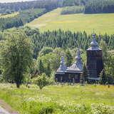 Cerkiew z trzema wieżami wśród wzgórz i drzew.