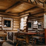 Wnętrze karczmy z drewnianych bali. Drewniane stoły i ławy, białe zdobienia wokół okien.