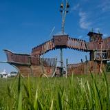 Duży drewniany statek do zabawy dla dzieci na tle błękitnego nieba i zielonej trawy.