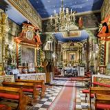 Wnętrze kościoła. Ołtarz główny z obrazem Matki Boskiej z Dzieciątkiem, kilka ołtarzy bocznych, drewniane ławki, ściany i sufit ozdobione malowidłami i obrazami.
