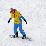 Mężczyzna w żółto-niebieskim komplecie sportowym zjeżdża na desce snowboardowej po ośnieżonym stoku