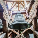 Trzy szare, zdobione dzwony zawieszone na skomplikowanej  konstrukcji z drewnianych bali.