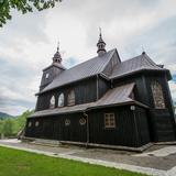 Drewniany, w ciemnym kolorze, kościół z dachem krytym blachą.