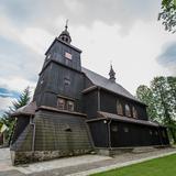 Drewniany, w ciemnym kolorze, kościół z wieżą nad wejściem.