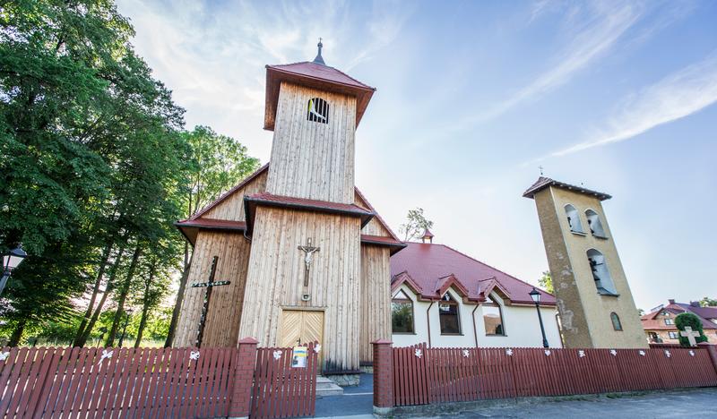 Drewniany kościół z wysoką wieżą nad wejściem. Obok murowana dzwonnica.