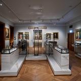 Sala muzealna z ekspozycją pamiątek rodziny Czartoryskich w szklanych gablotach pośrodku sali i obrazami na ścianach.