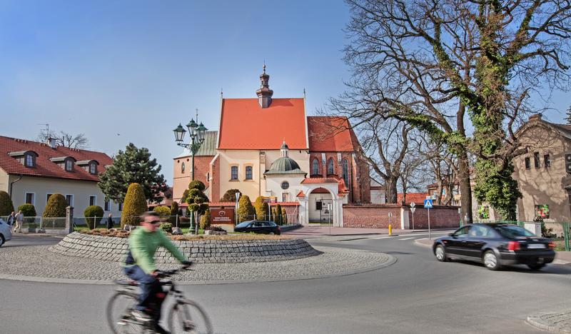 Niewielki kościół z cegły, częściowo pomalowany na jasny kolor, na pierwszym planie rowerzysta objeżdżający rondo