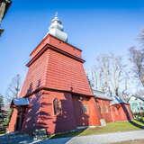 Drewniana cerkiew o ścianach w kolorze czerwonobrązowym i jasnym dachu. Na froncie wieża.