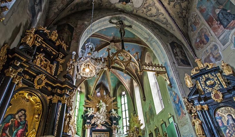 Wnętrze kościoła. Bogato zdobione ciemne ołtarze ze złotymi elementami. Malowidła na suficie i ścianach.