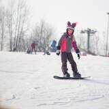 Dziewczynka na desce snowboardowej na stoku Podstolice Ski. Trasa jest wyratrakowana, a niebo dość pochmurne.