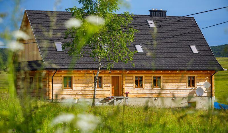 Drewniany dom wzorowany na autentycznej łemkowskiej chyży z jasnego drewna pod ciemnym gontem
