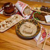 Drewniany stół, na nim zdobione talerze z potrawami i serwety z motywem łemkowskim