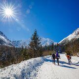 Turyści idący szlakiem nad orskie Oko zimą, w tle ośnieżone szczyty.