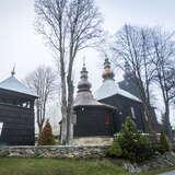 Drewniana cerkiew otoczona niskim murkiem, z przodu wolnostojąca dzwonnica. Widok zimowy.