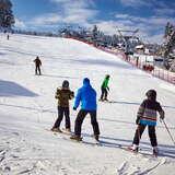 Nauka jazdy na nartach na stacji narciarskiej Henryk Ski w zimowy słoneczny dzień, w tle grupa narciarzy
