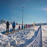 Grupa narciarzy korzystających z przenośnika taśmowego na stacji narciarskiej Master-Ski w Tyliczu, w tle widok na wyciąg krzesełkowy