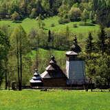 Kopuły i dachy drewnianej cerkwi widziane z oddali, wokoło krajobraz zielonych wzgórz.