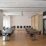 Sala konferencyjna z dwoma długimi stołami i krzesłami dookoła i rzędem krzeseł ustawionych pod ścianą