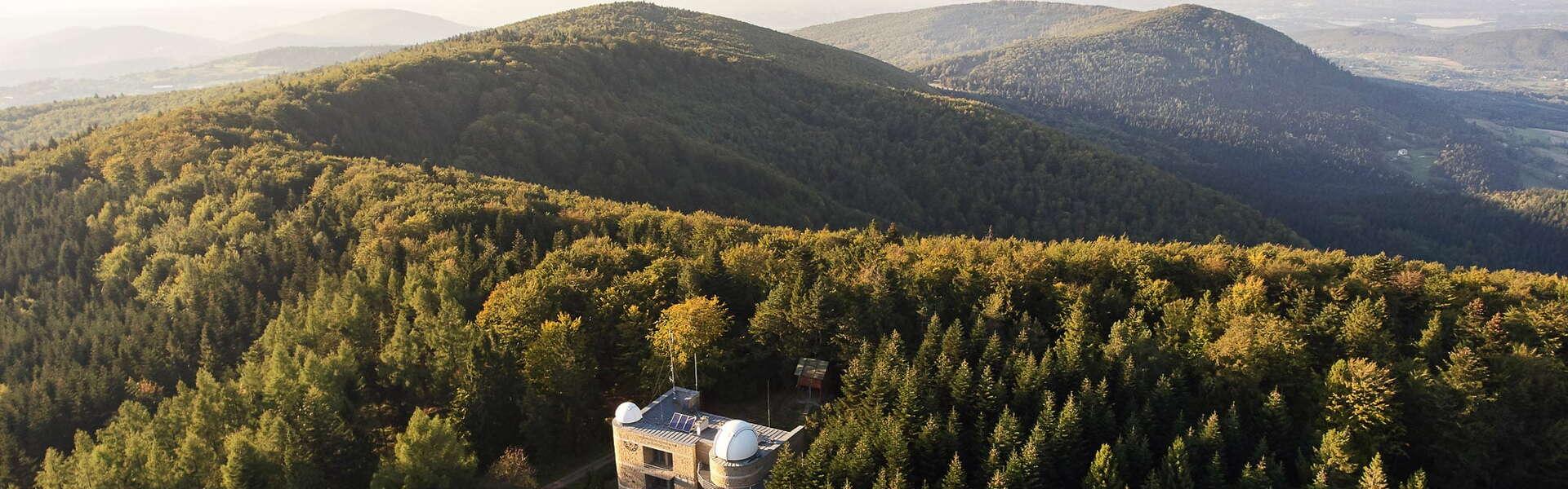 Obserwatorium astronomiczne na górze Lubomir. Wokół roztaczają się zielone połacie drzew