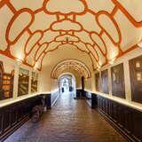 Korytarz w Kamienicy Szarej w Krakowie z galerią zdjęć. Okrągłe sklepienie jest ozdobione pomarańczowymi ornamentami. Po lewej stronie korytarza znajduje się stary rower.