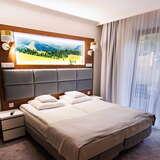 Jasny pokój z oknem balkonowym. Podwójne łóżko z szarym tapicerowanym zagłówkiem. Nad łóżkiem duże zdjęcie - panorama Beskidu Sądeckiego.