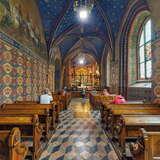 Nawa główna i ołtarz w Bazylice św. Franciszka w Krakowie. Po obu stronach  drewniane ławki, w niektórych z nich siedzą wierni. Ściany świątyni oraz sufit zdobione są malowidłami.