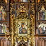 Obraz Matki Boskiej w złoconej ramie na ścianie drewnianego ołtarza w Sanktuarium Matki Bożej Nieustającej Pomocy w Krakowie. Obok obrazu po lewej złota róża. Po prawej i lewej obrazy z życia Matki Bożej.