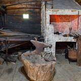 Pomieszczenie z piecem, licznymi starymi narzędziami oraz miejscem do rąbania drewna w starej, ciemnej chacie w Muzeum PTTK Skansen w Dobczycach.