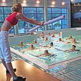 Instruktorka aerobiku stojąca nad basenem i pokazująca ćwiczenia, uczestniczki w basenie.