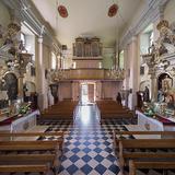 Wnętrze kościoła, jasne ściany, posadzka w szachownicę, organy na chórze, barokowe ołtarze boczne, drewniane ławy.