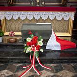 Sarkofag przykryty biało-czerwona flagą, kwiaty.