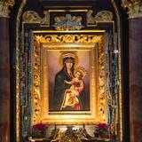 Obraz Madonny z Dzieciątkiem w złotej ramie. Wizerunek przykryty sukienkami i koronowany. Ołtarz czarny, złocony.
